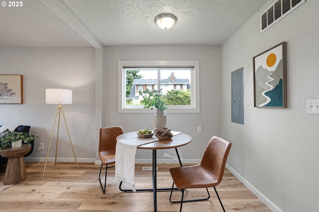 dining area featuring electric panel, light wood-style floors, a textured ceiling, and baseboards