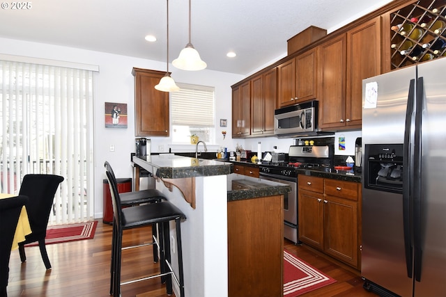 kitchen featuring dark wood-style flooring, hanging light fixtures, stainless steel appliances, recessed lighting, and a center island with sink