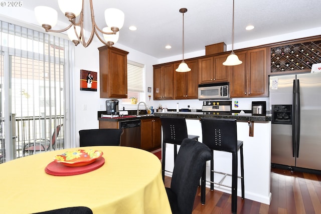 kitchen with pendant lighting, dark countertops, appliances with stainless steel finishes, dark wood-style floors, and a notable chandelier