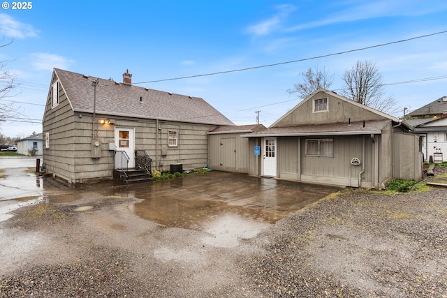 back of property featuring an outbuilding, driveway, roof with shingles, and a chimney