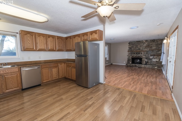 kitchen featuring light hardwood / wood-style floors, ceiling fan, appliances with stainless steel finishes, a fireplace, and a textured ceiling