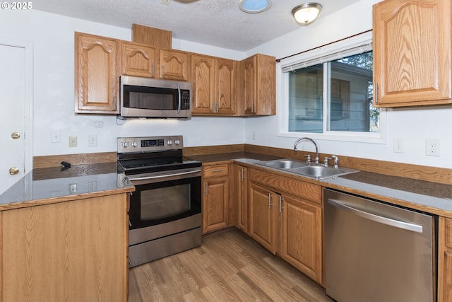 kitchen with sink, a textured ceiling, appliances with stainless steel finishes, and light hardwood / wood-style flooring