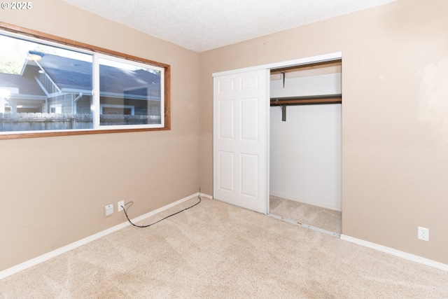 unfurnished bedroom featuring light colored carpet, a textured ceiling, and a closet