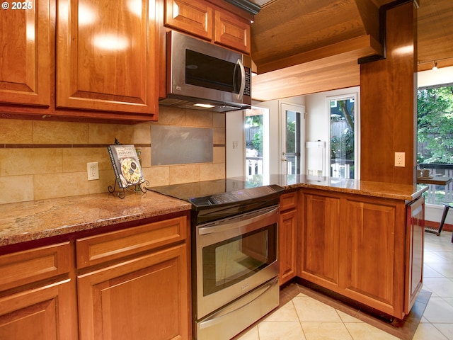 4214 NE Hassalo St, Portland, OR 97213 - kitchen featuring stainless steel appliances, brown cabinetry, light tile patterned flooring, backsplash, and light stone counters