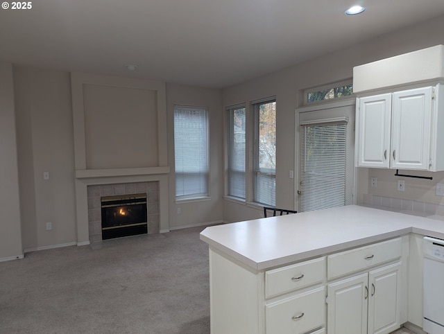 kitchen with white cabinets, a fireplace, kitchen peninsula, white dishwasher, and light colored carpet