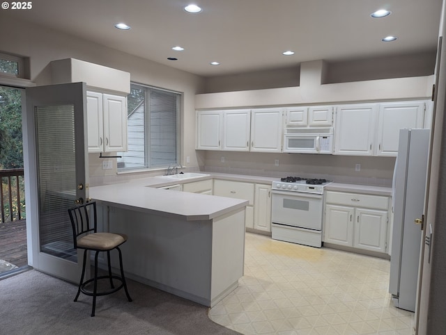 kitchen with white appliances, white cabinetry, sink, a kitchen breakfast bar, and kitchen peninsula