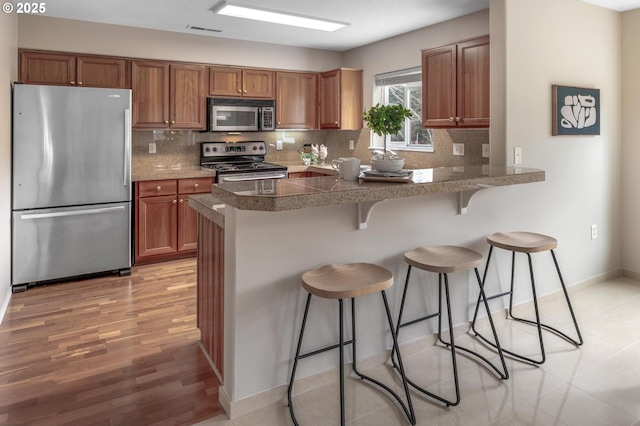 30326 SW Ruth St Unit 58, Wilsonville, OR 97070 - kitchen featuring stainless steel appliances, a breakfast bar, decorative backsplash, and brown cabinetry