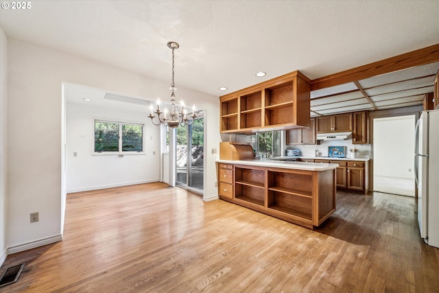 kitchen featuring kitchen peninsula, decorative light fixtures, white refrigerator, light hardwood / wood-style floors, and a chandelier