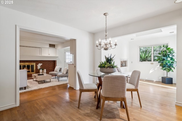 4401 SW Westdale Dr, Portland, OR 97221 - dining room with a brick fireplace, a healthy amount of sunlight, a chandelier, and light wood-type flooring