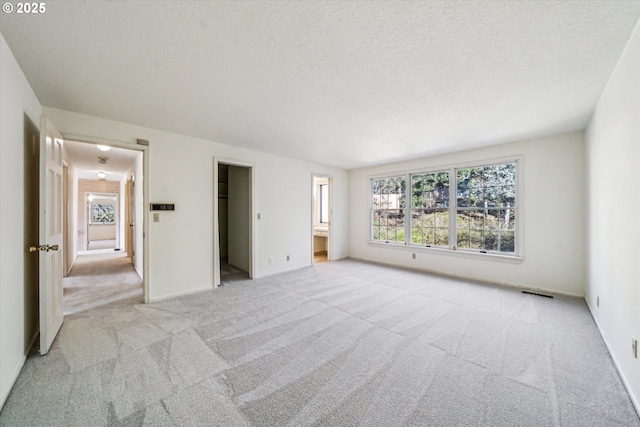 unfurnished bedroom featuring ensuite bath, light carpet, a textured ceiling, and a spacious closet