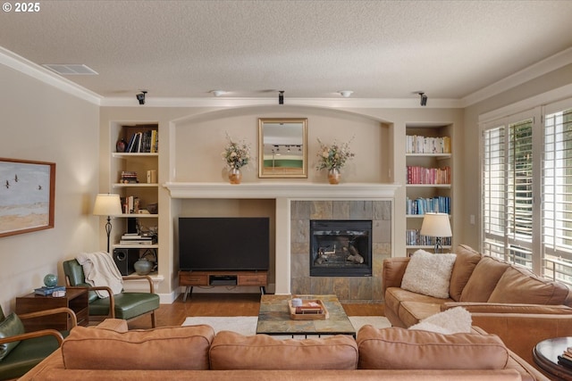 living area featuring crown molding, a tiled fireplace, wood finished floors, a textured ceiling, and built in features