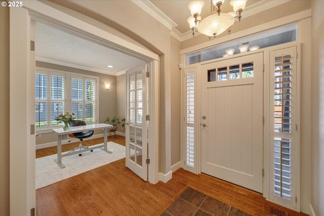 foyer featuring baseboards, a notable chandelier, wood finished floors, and ornamental molding