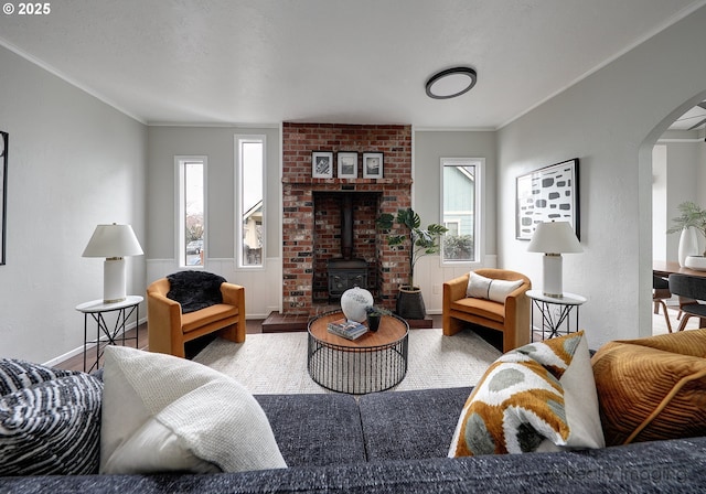 living room with wood finished floors, arched walkways, crown molding, baseboards, and a wood stove