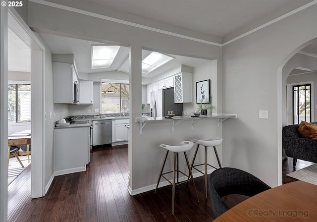 kitchen with white cabinetry, arched walkways, appliances with stainless steel finishes, a peninsula, and dark wood-style flooring