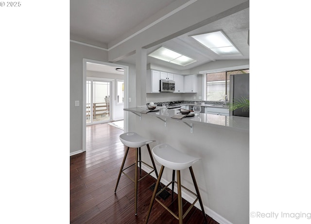 kitchen with dark wood-type flooring, stainless steel microwave, white cabinetry, freestanding refrigerator, and a breakfast bar area