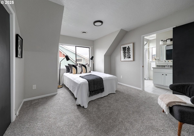 bedroom with baseboards, a sink, a textured ceiling, light colored carpet, and connected bathroom