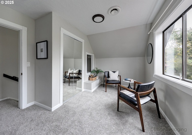 sitting room with vaulted ceiling, carpet flooring, baseboards, and a textured ceiling