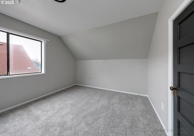 additional living space featuring vaulted ceiling, carpet flooring, baseboards, and a textured ceiling