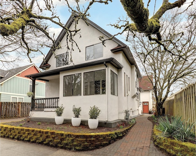 view of front of house with stucco siding, a porch, and fence