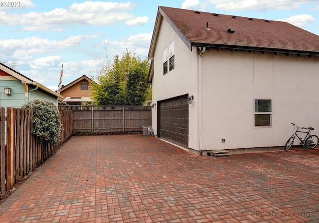 view of property exterior with decorative driveway, fence, a garage, and stucco siding