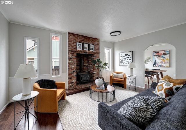 living room with crown molding, a wood stove, wood finished floors, and arched walkways