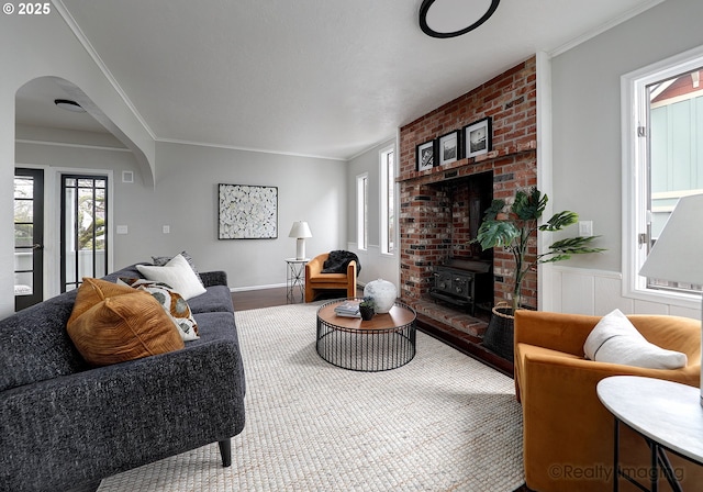 living room with crown molding, a wood stove, wood finished floors, and arched walkways