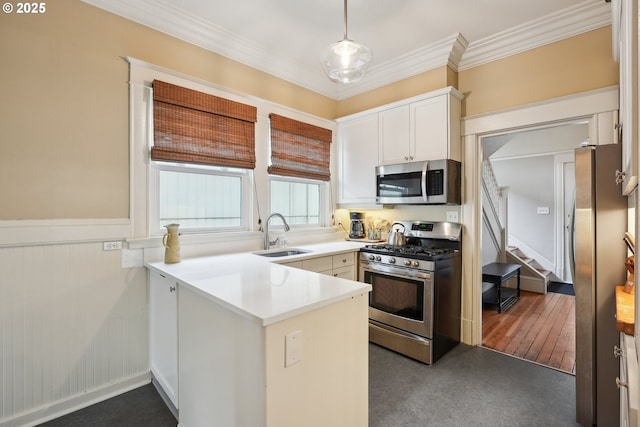 kitchen with appliances with stainless steel finishes, a sink, wainscoting, a peninsula, and white cabinetry