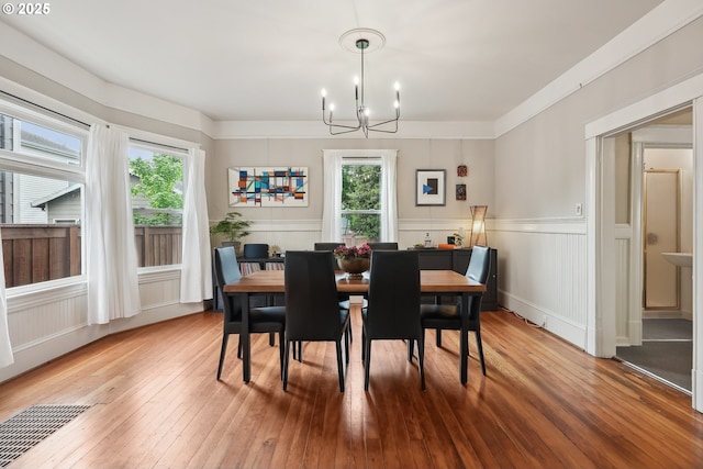 dining area featuring a chandelier, wood-type flooring, a wainscoted wall, and a decorative wall