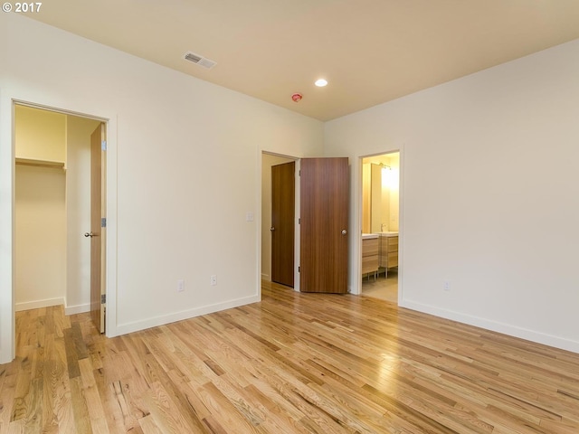 unfurnished bedroom featuring light wood-type flooring, baseboards, visible vents, and a walk in closet