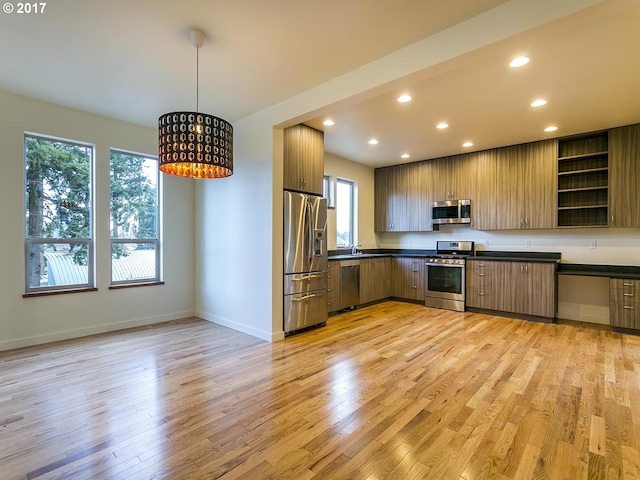 kitchen featuring light wood-style flooring, modern cabinets, stainless steel appliances, and decorative light fixtures