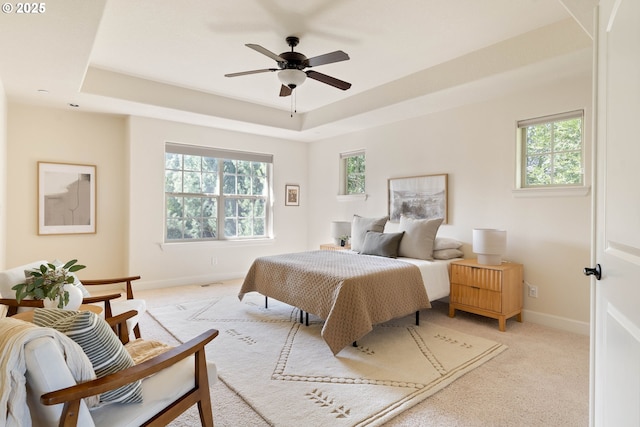 bedroom featuring a tray ceiling, baseboards, multiple windows, and light colored carpet