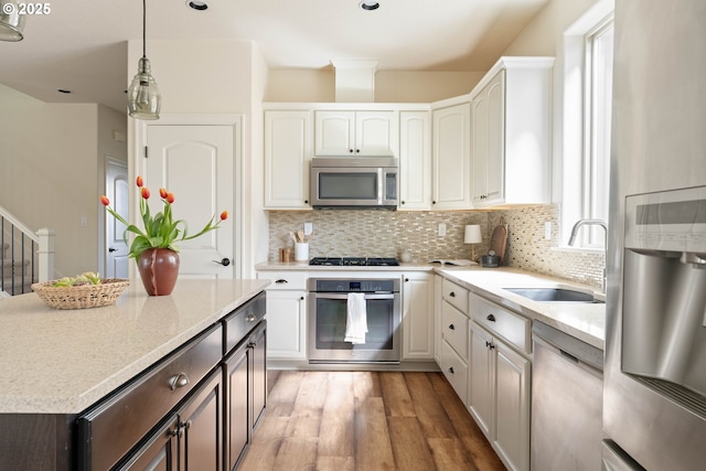 kitchen featuring tasteful backsplash, light wood-type flooring, white cabinetry, a sink, and stainless steel appliances