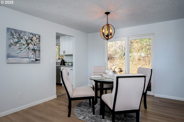 dining room featuring wood finished floors, a textured ceiling, baseboards, and an inviting chandelier