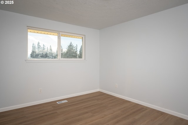 empty room with a textured ceiling, wood finished floors, visible vents, and baseboards