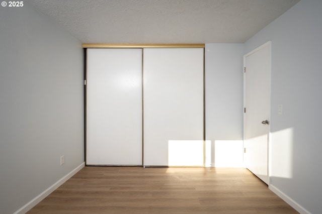 unfurnished bedroom featuring a closet, a textured ceiling, baseboards, and wood finished floors