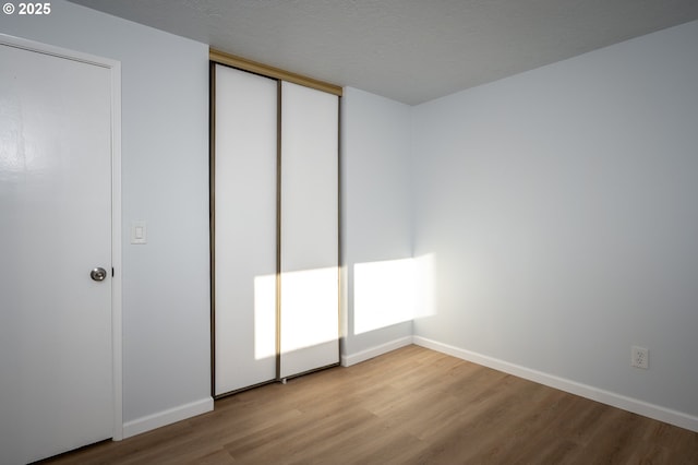 unfurnished bedroom featuring a closet, a textured ceiling, baseboards, and wood finished floors