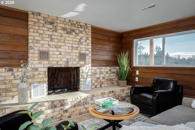 living area with a brick fireplace, visible vents, wooden walls, and wood finished floors