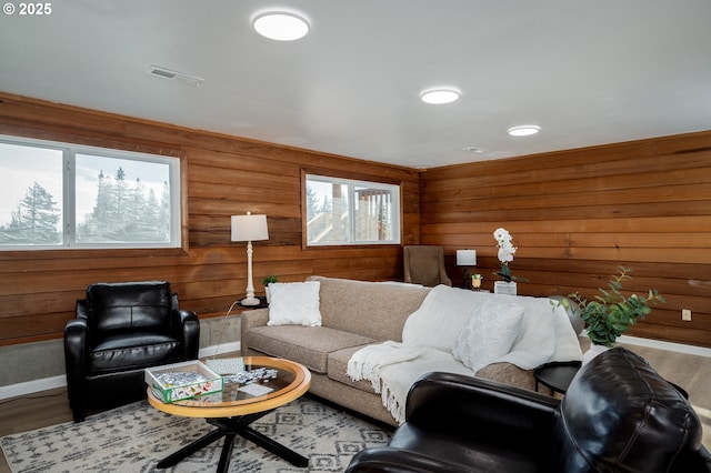 living area featuring visible vents, wood walls, baseboards, and wood finished floors