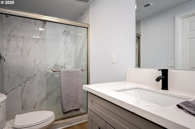 bathroom featuring a textured wall, toilet, visible vents, vanity, and a marble finish shower