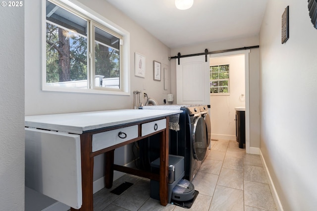 laundry area featuring laundry area, washing machine and clothes dryer, a barn door, light tile patterned floors, and baseboards