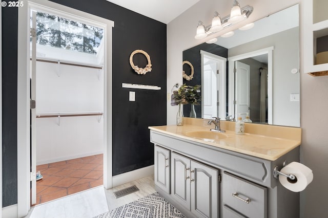 bathroom with baseboards, visible vents, a walk in closet, and vanity