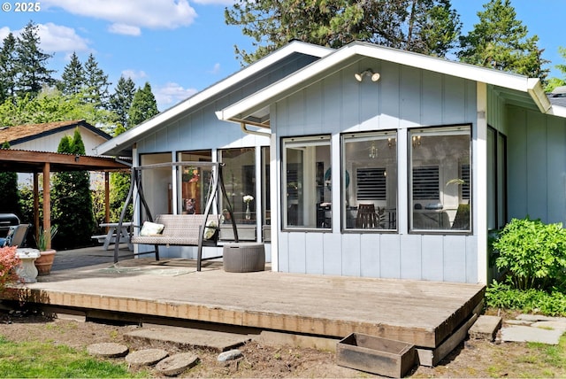 rear view of house with board and batten siding, a wooden deck, and a sunroom