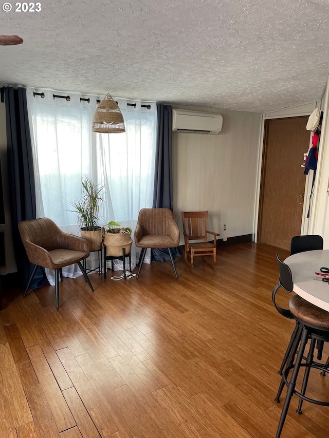 sitting room with a wall mounted air conditioner, hardwood / wood-style flooring, and a textured ceiling