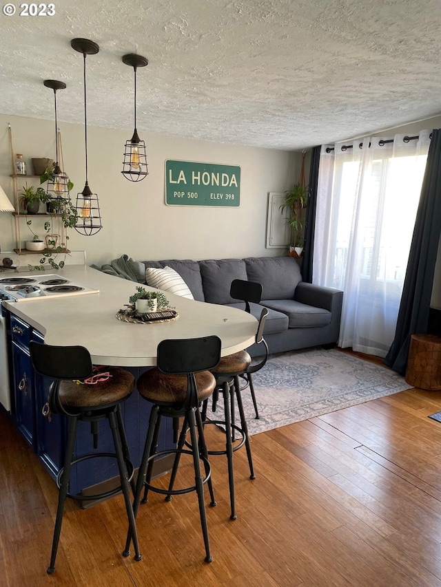 interior space featuring blue cabinets, decorative light fixtures, a breakfast bar area, and wood-type flooring