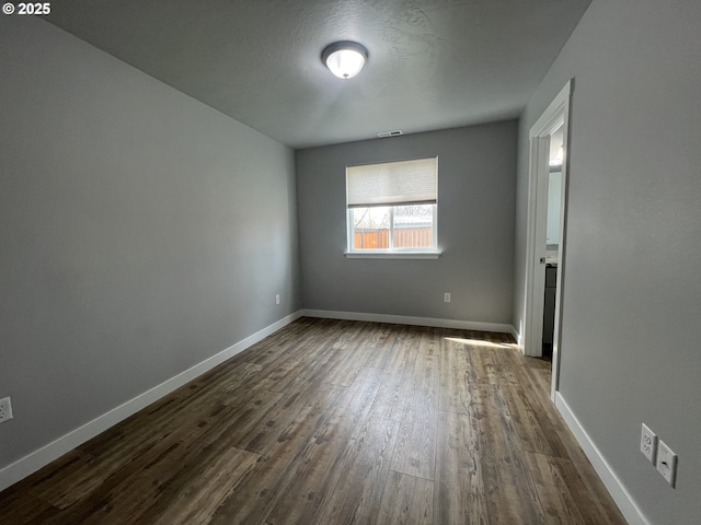empty room with dark wood finished floors, baseboards, and visible vents