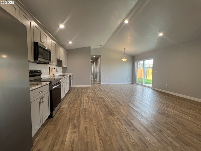 kitchen featuring stainless steel appliances, vaulted ceiling, a sink, and dark wood-type flooring