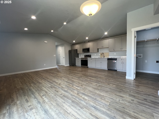 kitchen featuring wood finished floors, a sink, baseboards, lofted ceiling, and appliances with stainless steel finishes