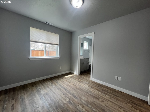 unfurnished bedroom with dark wood-style flooring, baseboards, visible vents, and multiple windows