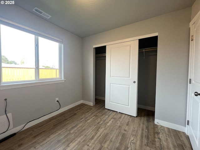unfurnished bedroom with baseboards, wood finished floors, visible vents, and a closet