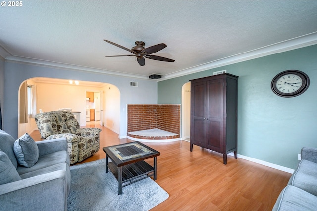 living room featuring arched walkways, a textured ceiling, crown molding, and light wood finished floors